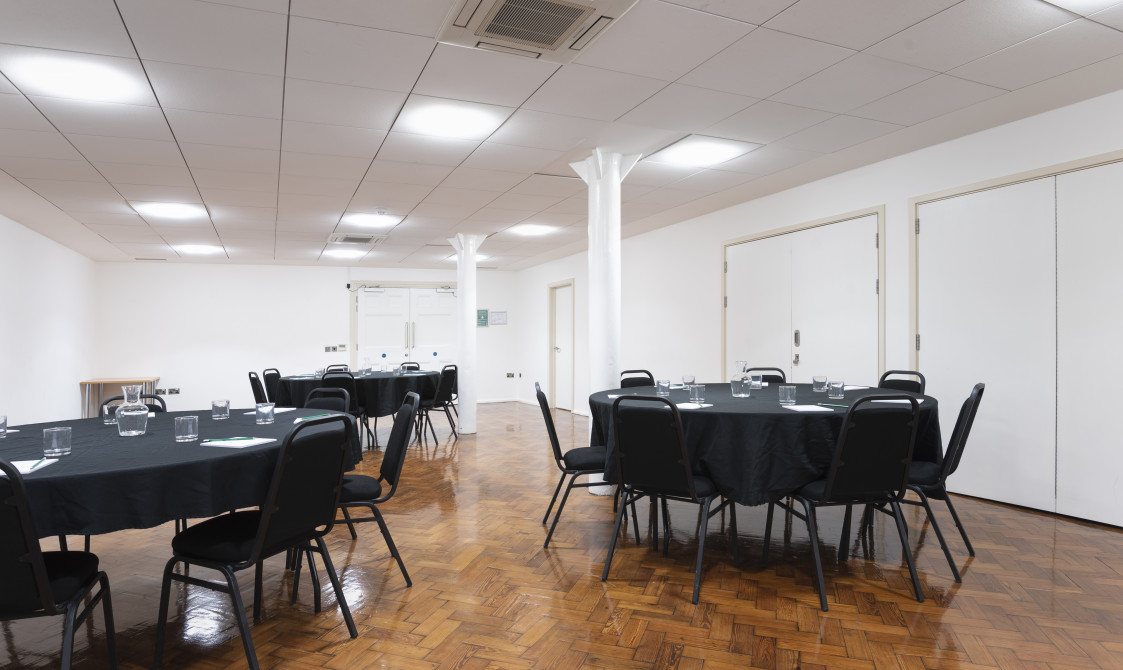 A photograph of the Goss Room at Bishopsgate Institute London. The tables are set out in a cabaret style with chairs around them.