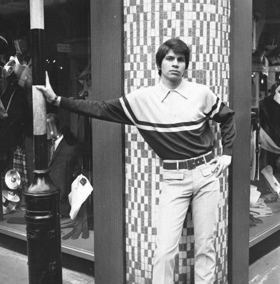 A Black and white photo of a male model posing outside a clothing shop on Carnaby Street in the 1960s