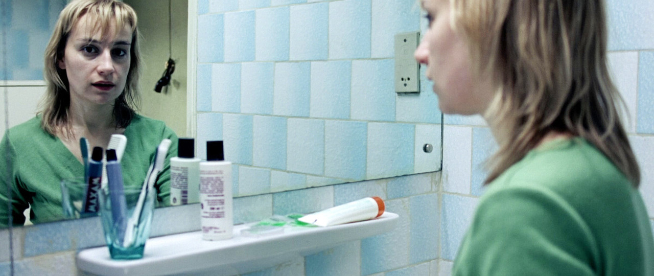 Imagine of a woman looking into the camera through the reflection of a bathroom mirror.