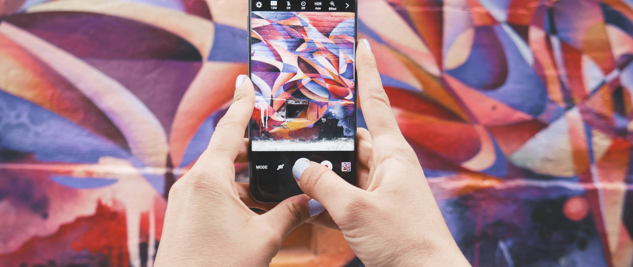 Imagine of an iPhone capturing a picture of an abstract mural on a brick wall.