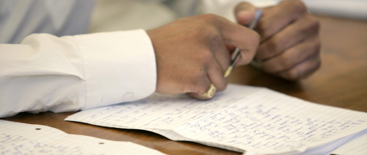 The shot focuses on someone's hands, who is holding a pen, preparing to write on the paper in front of them.