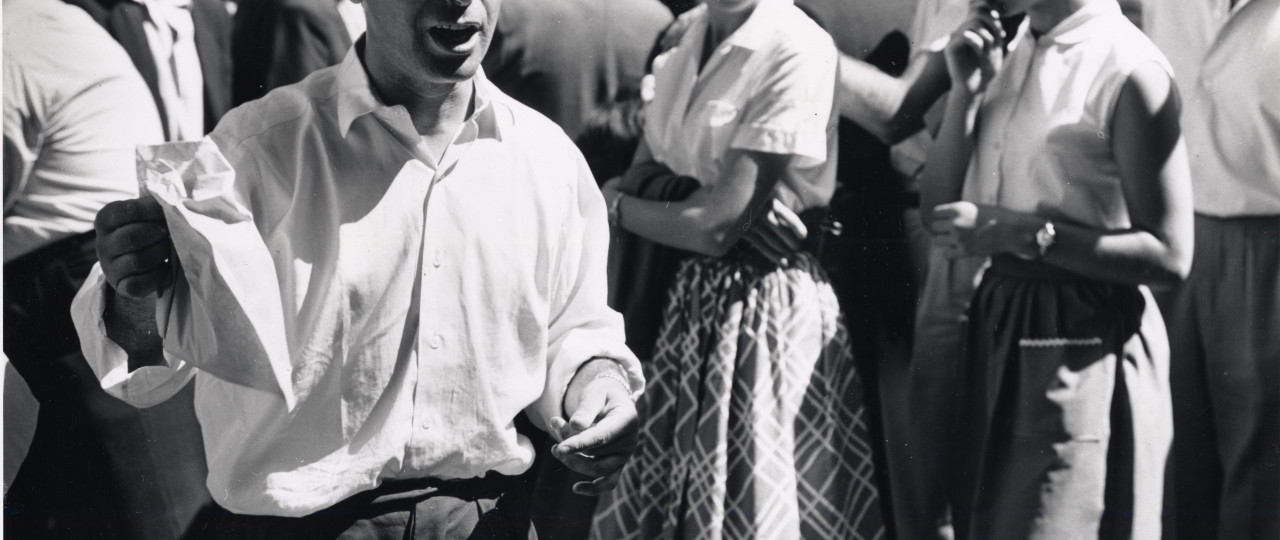 Photo from our collection of a man holding a paper bag, stood with a crowd behind him.