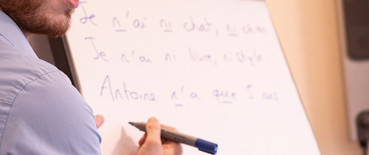 A tutor teaching a French course at Bishopsgate Institute. He is writing different French phrases on the flipchart.