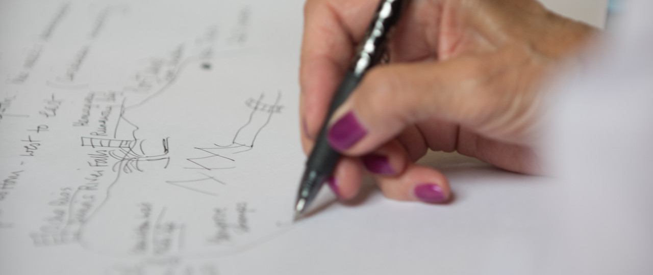 A woman is writing on a piece of paper with a black pen. The pen is in her right hand, and the rest of the image is out of focus.a