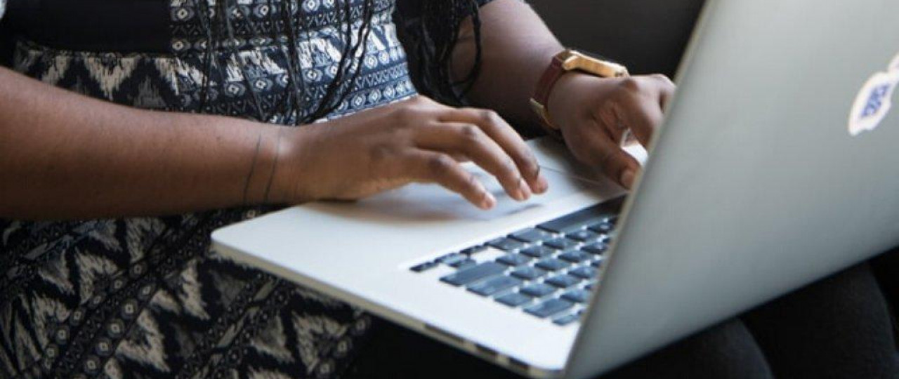 A woman is typing on a laptop. The image focuses on her hands and the keypad.