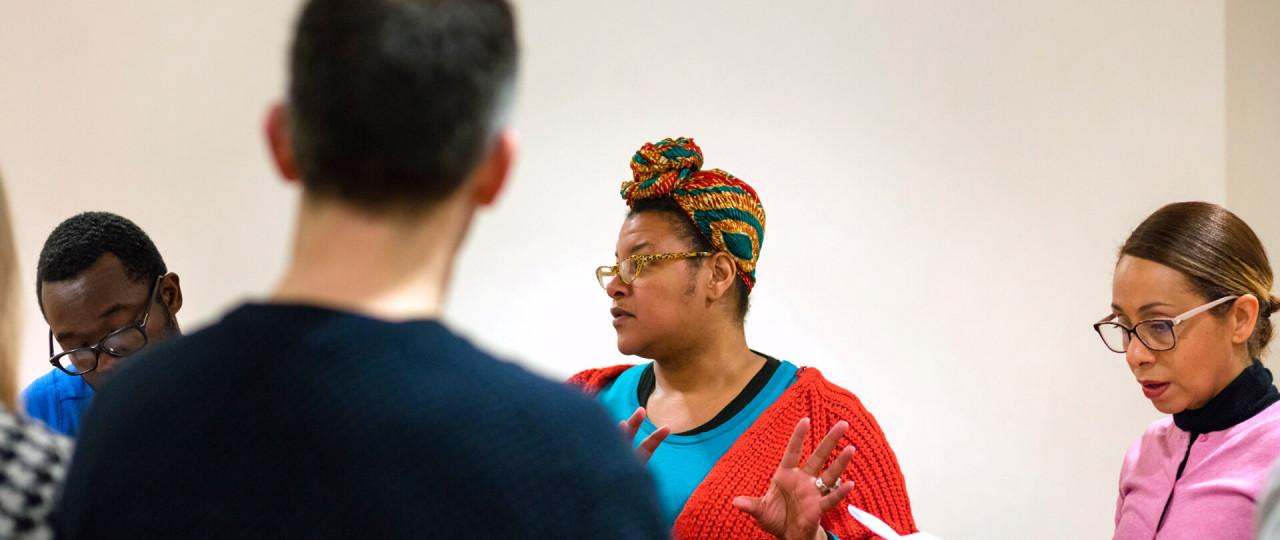 Jennifer Farmer is teaching a playwriting course, with students sitting around her, holding pieces of paper.