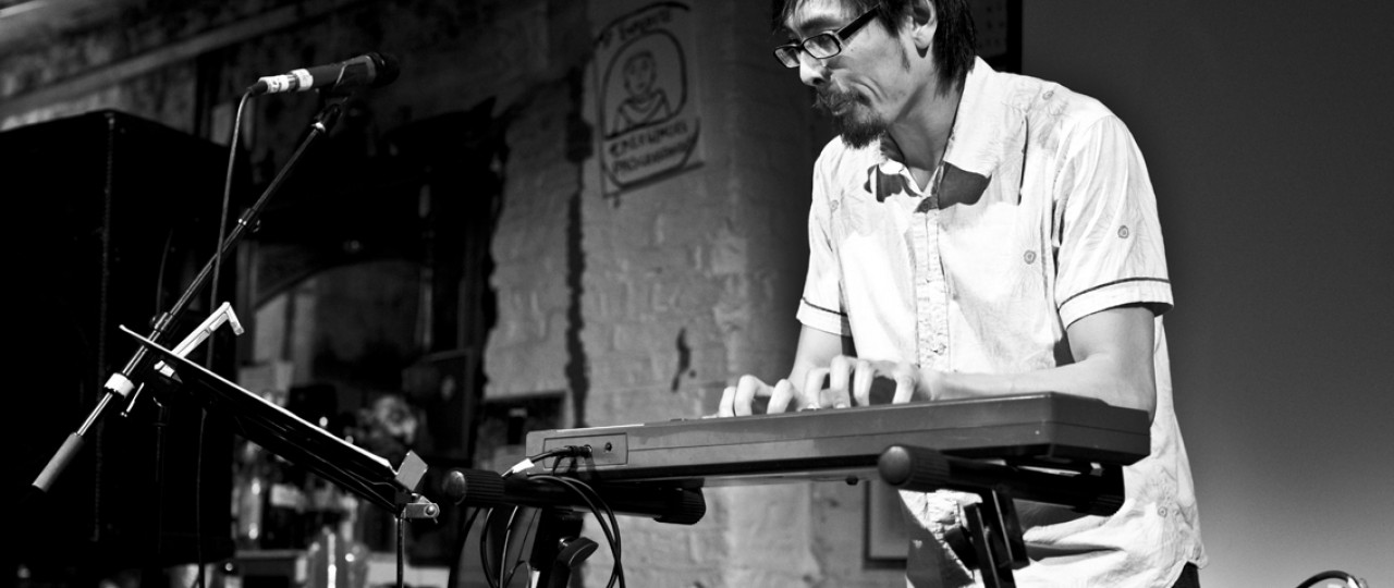 Performer Kerry Young is playing the keyboard on stage, with a microphone in front of him.