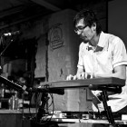Performer Kerry Young is playing the keyboard on stage, with a microphone in front of him.