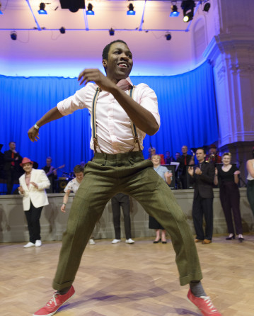 Image from our collection of a man Swing dancing with a brace on and a group of people watching on from behind.