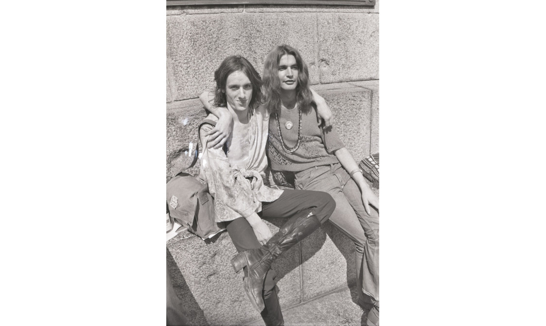 A picture from the second Pride march in 1973. Two people are sitting down on the steps at Embankment, with their arms wrapped around each other.