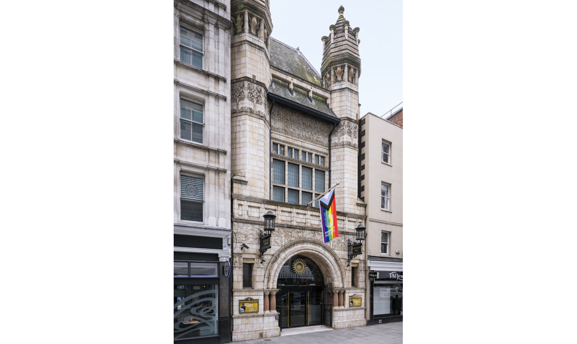 A photograph of Bishopsgate Institute's exterior. The building has two turrets and a domed entrance with the LGBTQ+ flag outside.