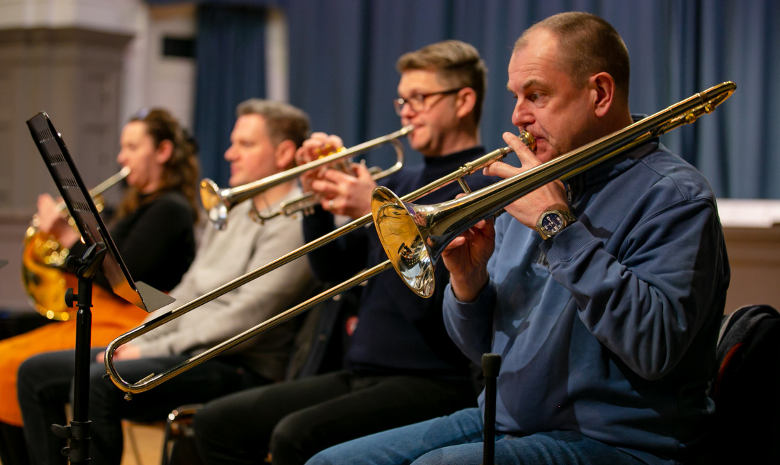 Four musicians are playing in Bishopsgate Institute's Great Hall. Two are playing the trombone and one is playing the tuba.
